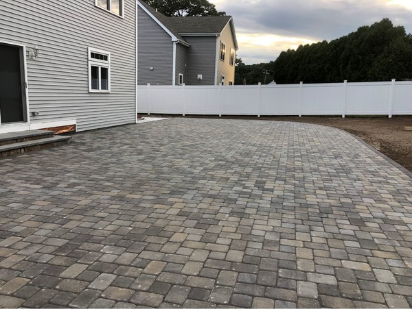 Paver patio installed beside a house with a white fence in the backyard